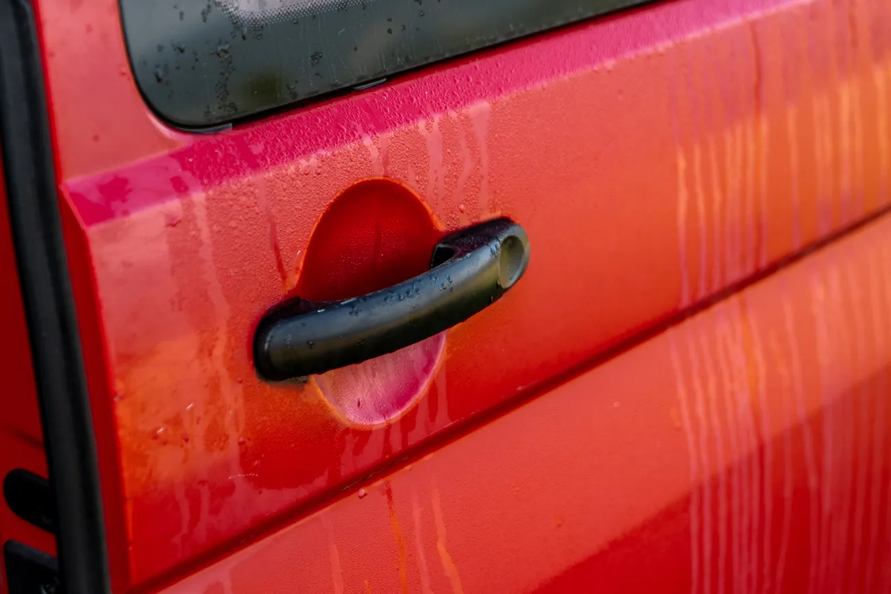 rote auto-tür mit schwarzem hebel und wassertröpfchen