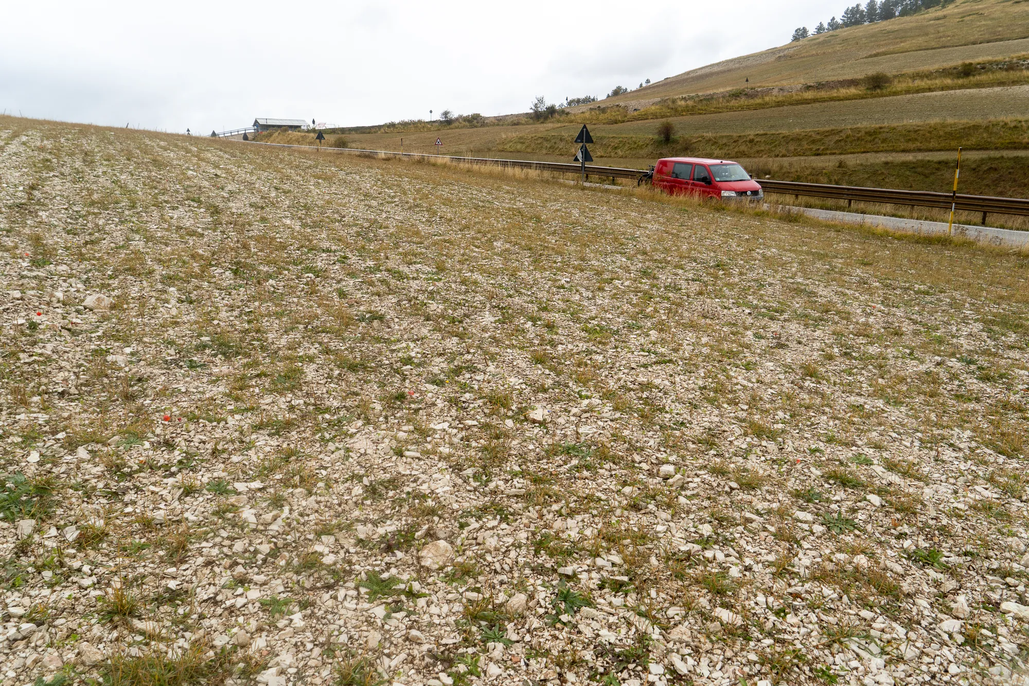 Steiniger Hang mit rotem Auto und Straße im Hintergrund