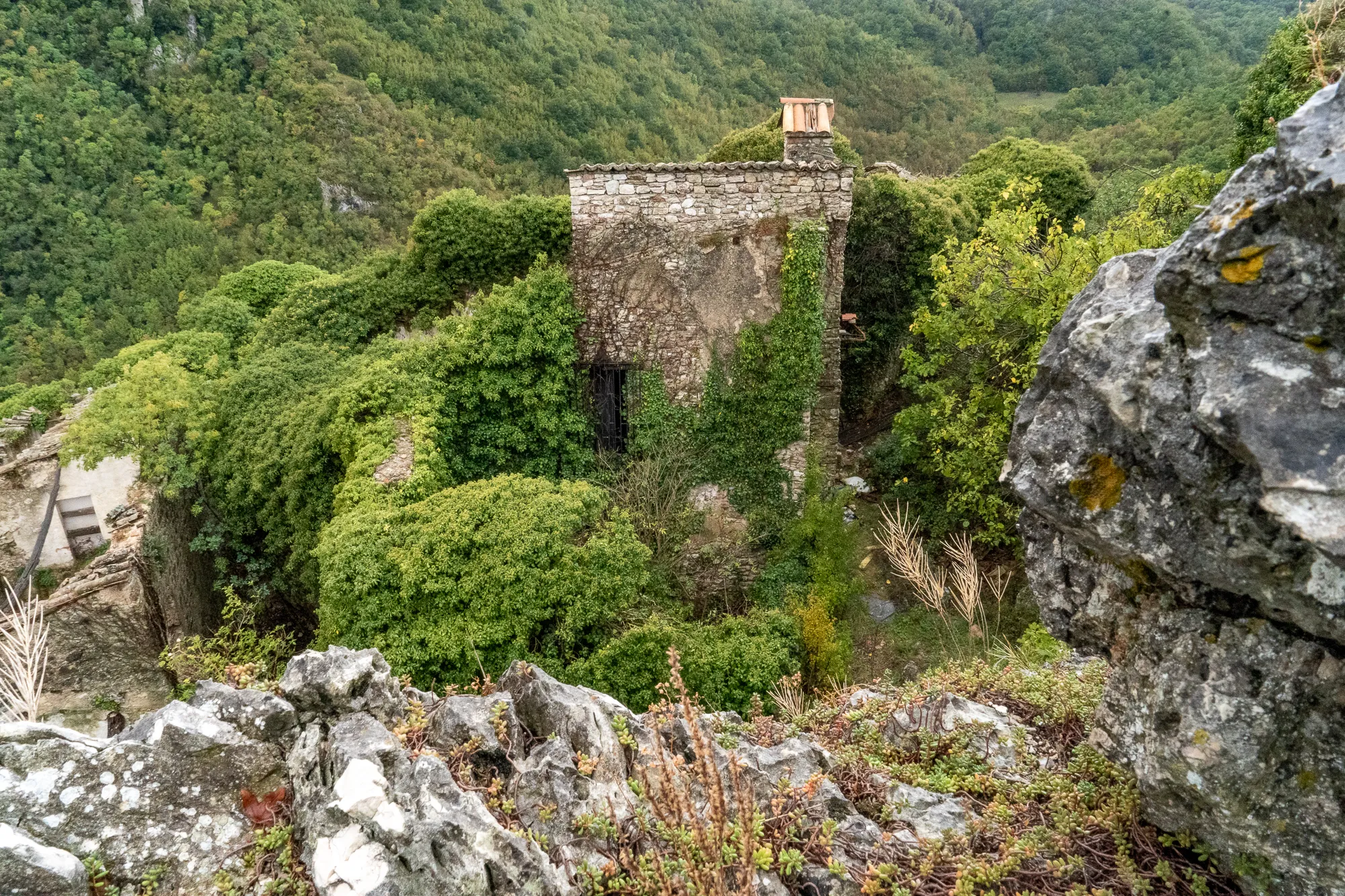 Verfallene Steinruine in dichtem Grün, umgeben von Felsen und Wald.