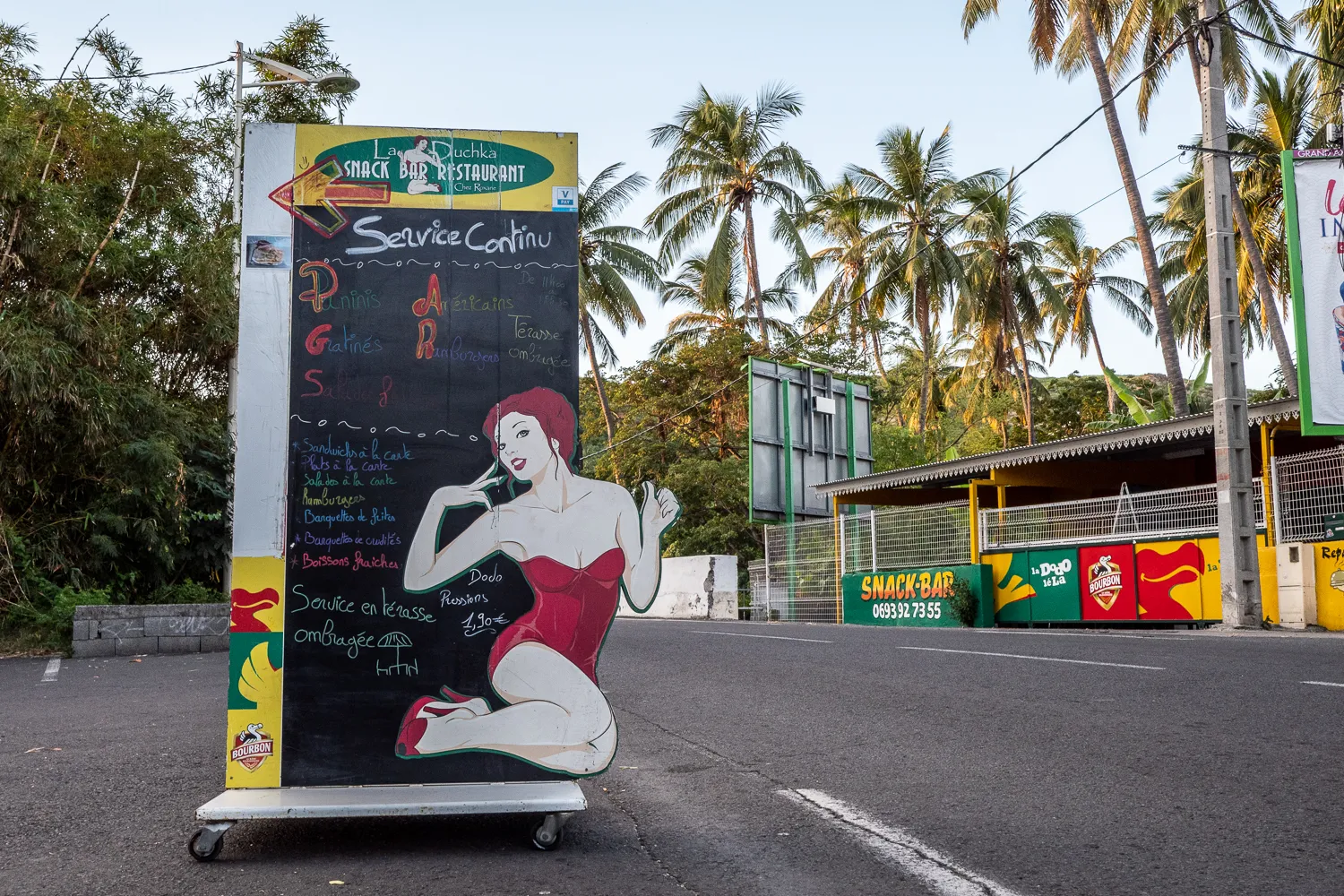 Schild mit Zeichnung einer Frau in rotem Kleid vor Palmen