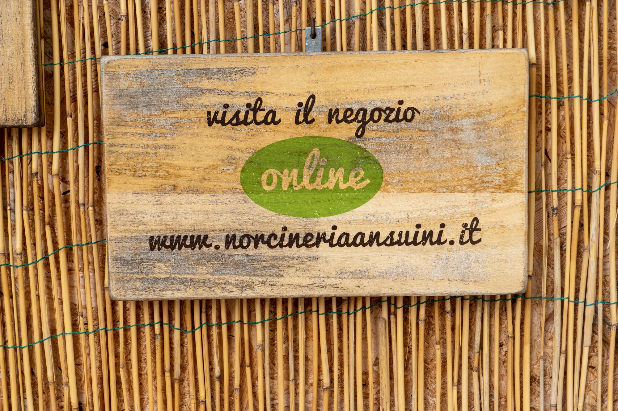 Holzschild mit Schriftzug und grünem Online-Logo an Bambuswand