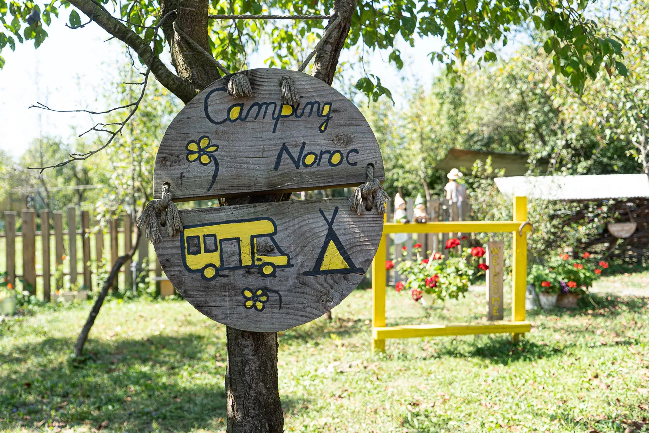 Holzschild mit Camping Noroc, Wohnmobil und Zelt, im Garten unter Bäumen