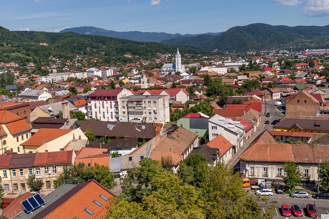 Stadtansicht mit roten Dächern, Kirche und Bergen im Hintergrund