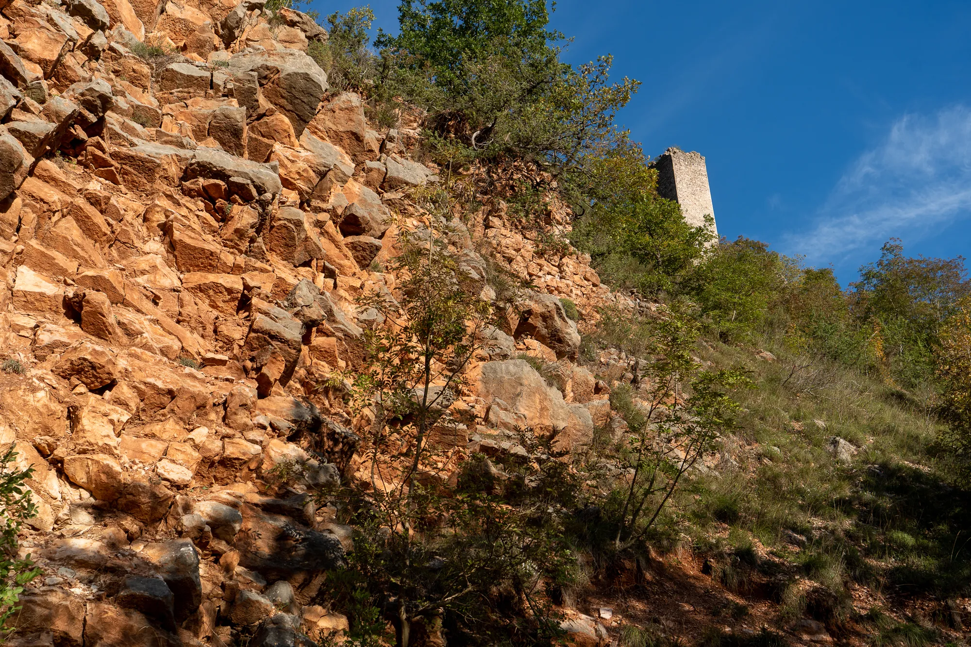 Steile Felswand mit Steinruine unter blauem Himmel