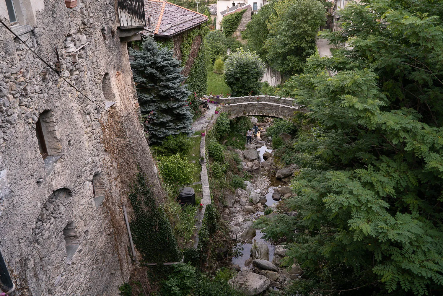 Alter Steinbau mit Arkaden, kleiner Fluss und Brücke im Grünen.