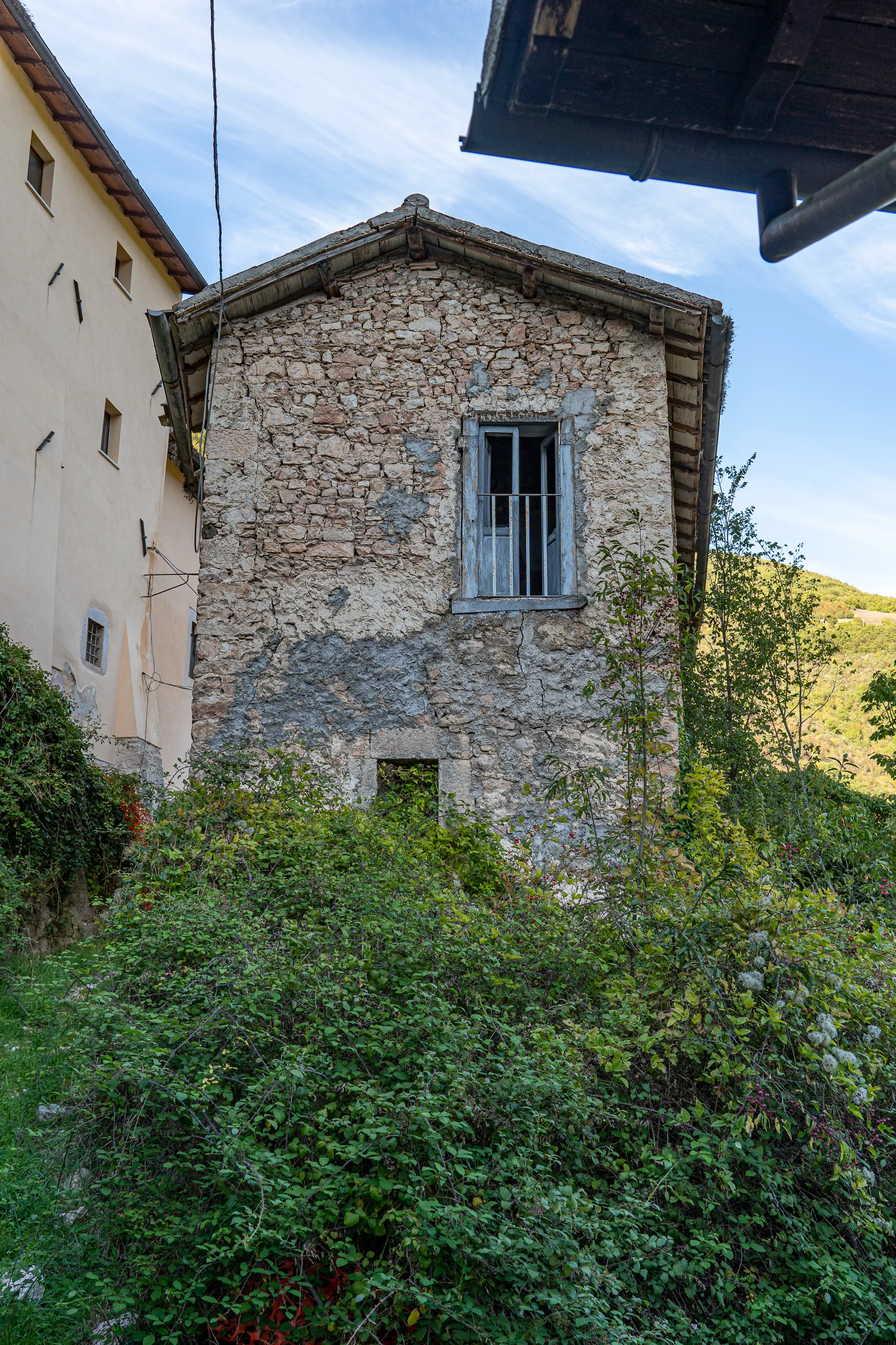 Alter Steinbau mit Fenster, umgeben von dichtem Grün und blauem Himmel