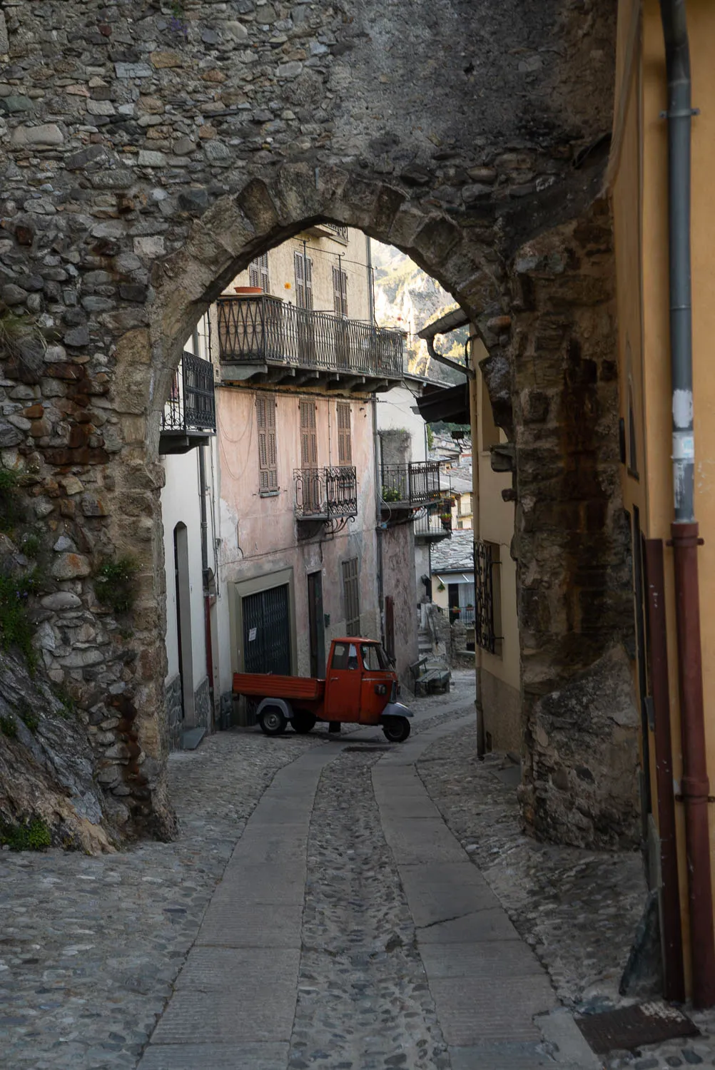 Steinbogen über schmale Gasse mit rotem Dreirad und alten Häusern
