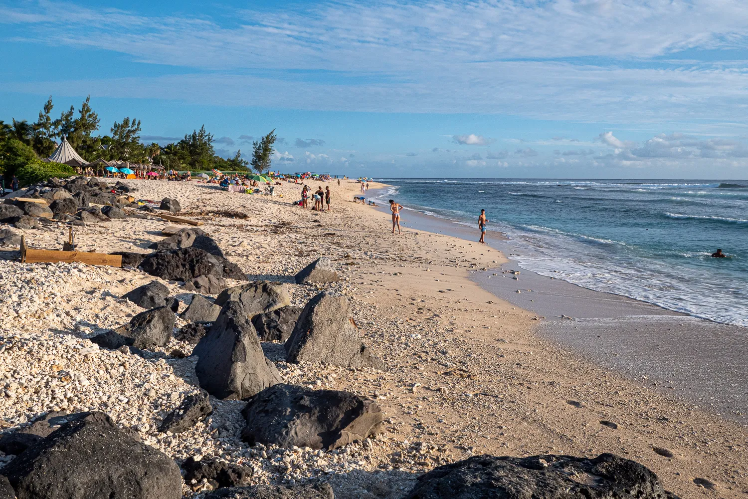 Strand mit Steinen, Wellen und Menschen unter blauem Himmel