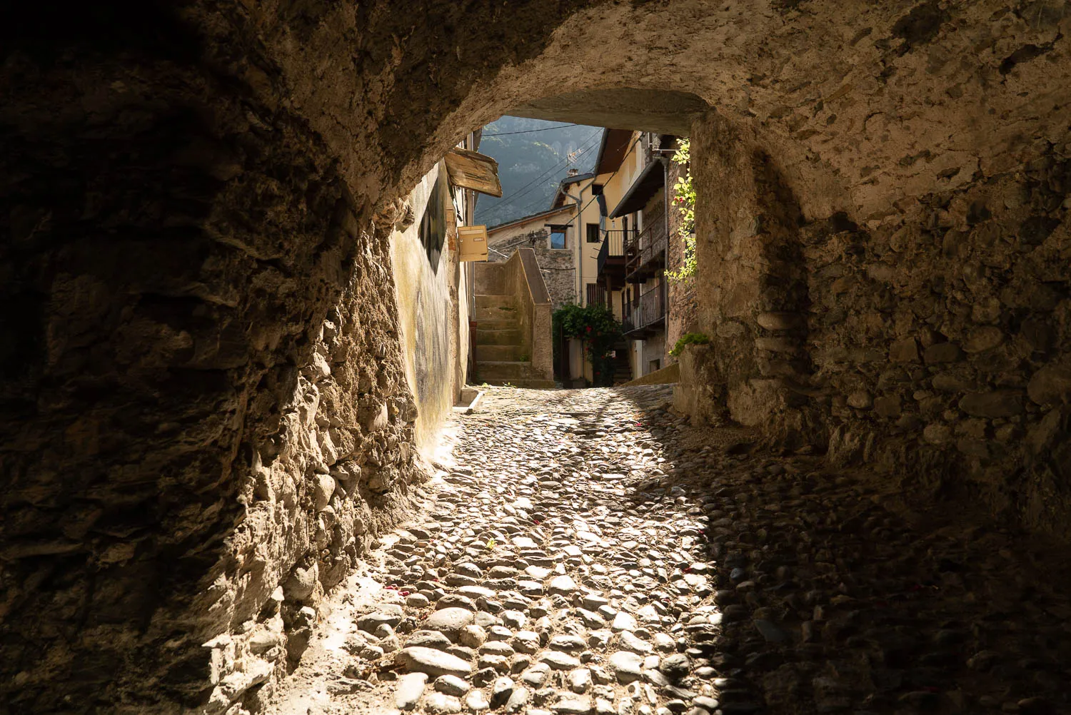 Steinweg durch Bogen in alte Stadtmauer, Sonnenlicht fällt auf Kiesbank