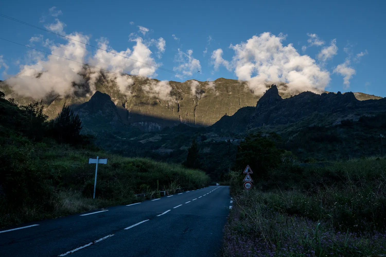 Straße durch bewaldete Berge mit Wolken und Straßenschildern
