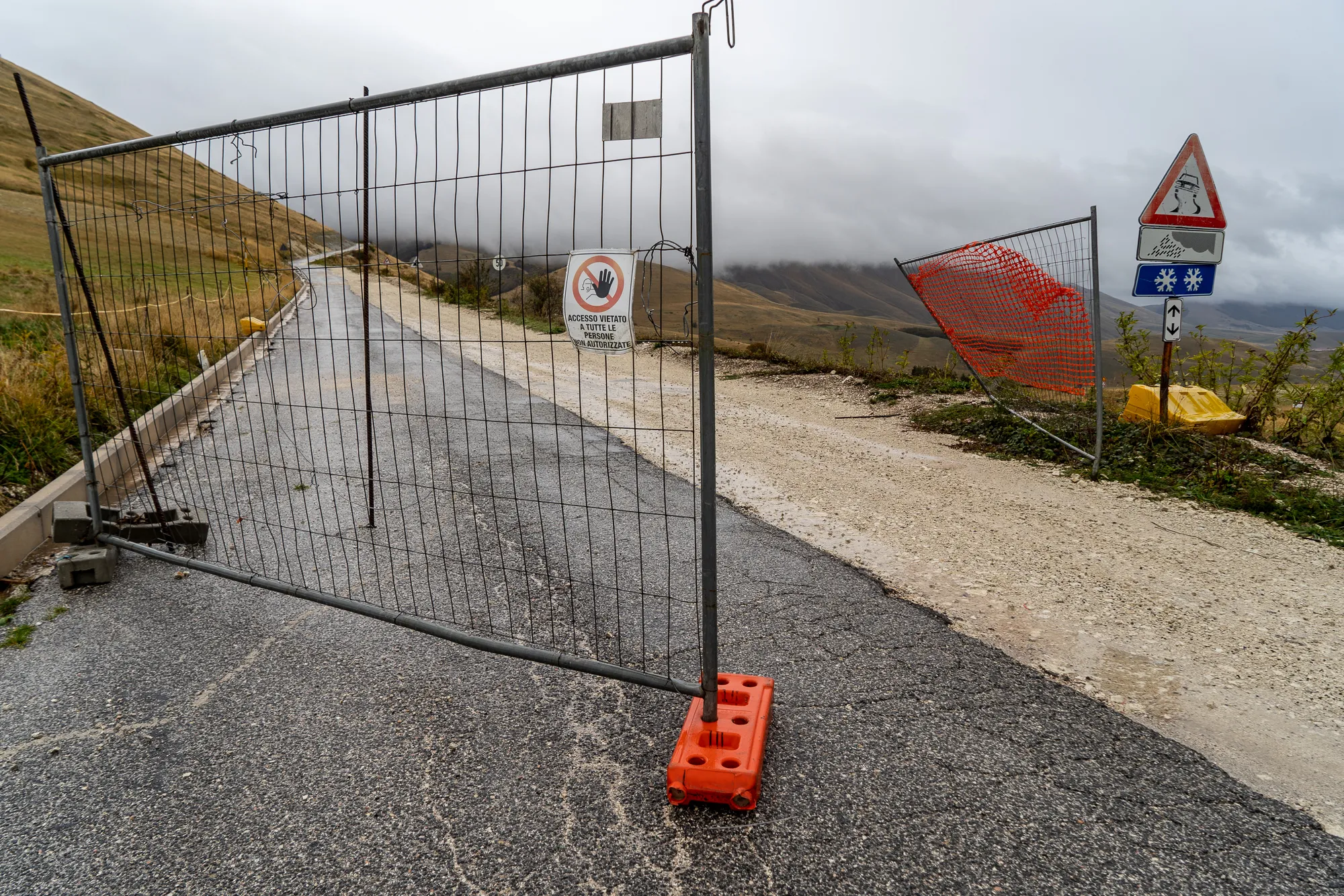 Gesperrte Straße mit Bauzaun und Warnschildern in bergiger Landschaft