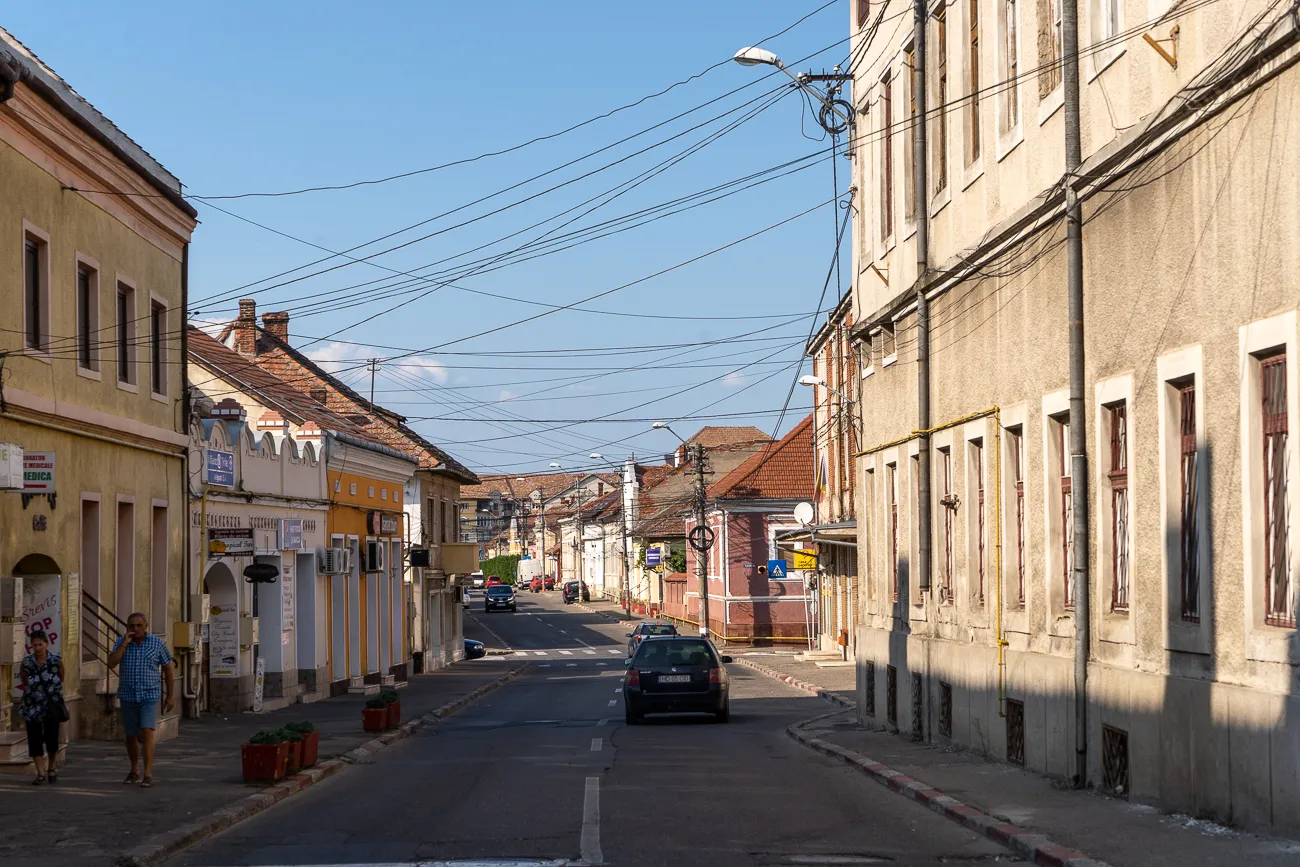 Straße mit Häusern, Autos und Passanten unter blauem Himmel.