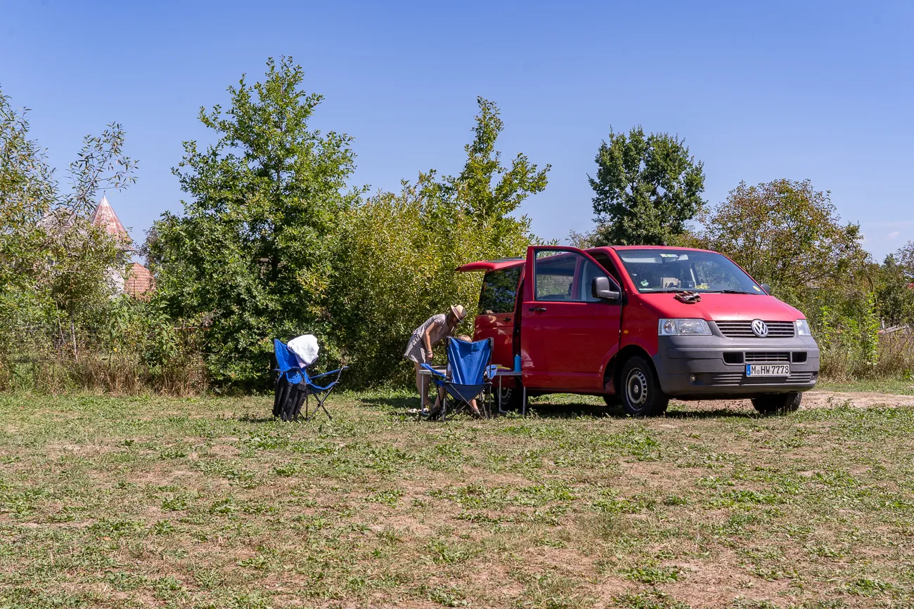 Mann stellt blaue Campingstühle neben rotem Van auf Grasfläche