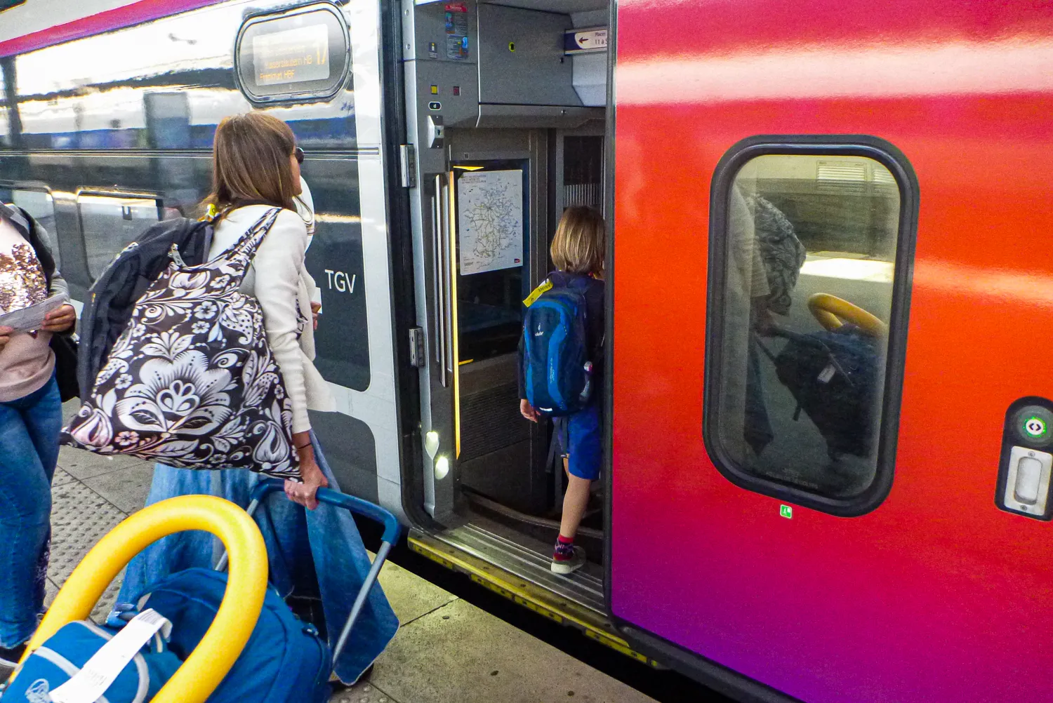 Reisende steigen in einen roten TGV-Zug ein, Kinder mit Rucksack und Koffer.