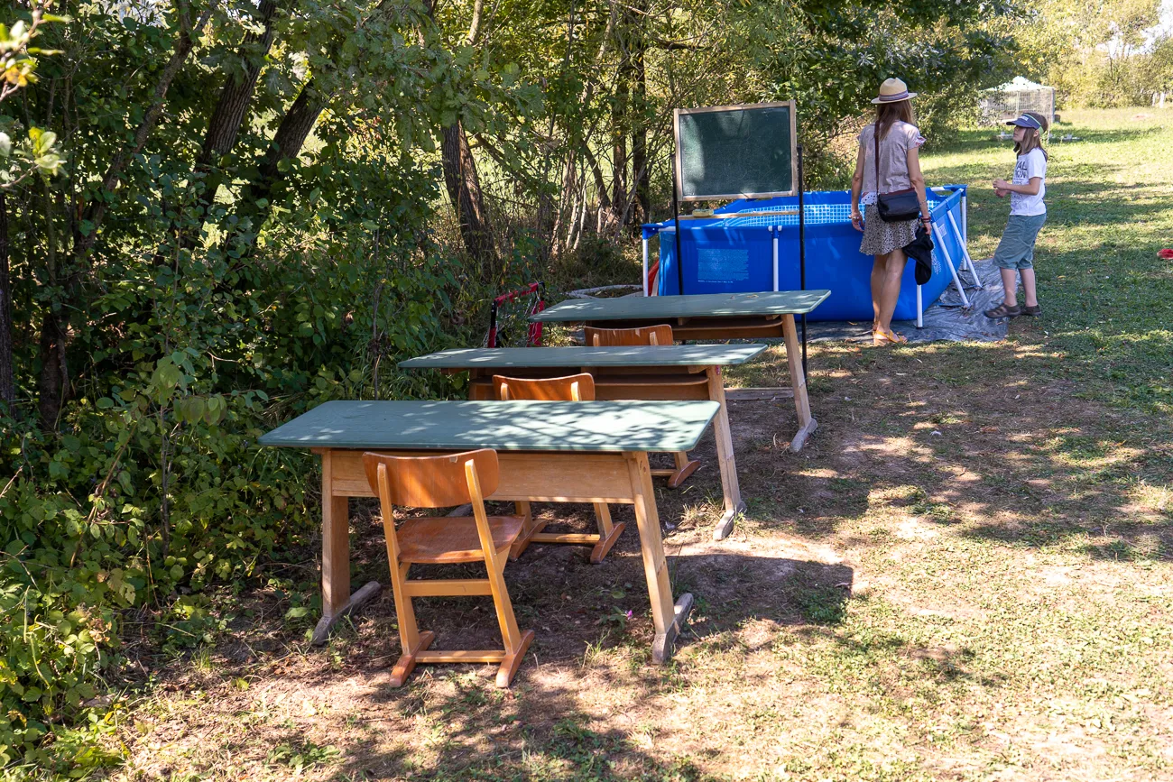 Holztische und Stühle im Gras, zwei Personen neben blauem Pool