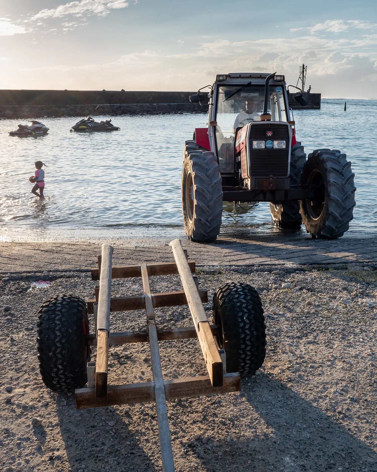 Traktor am Strand mit Kind im Wasser und Jetskis im Hintergrund