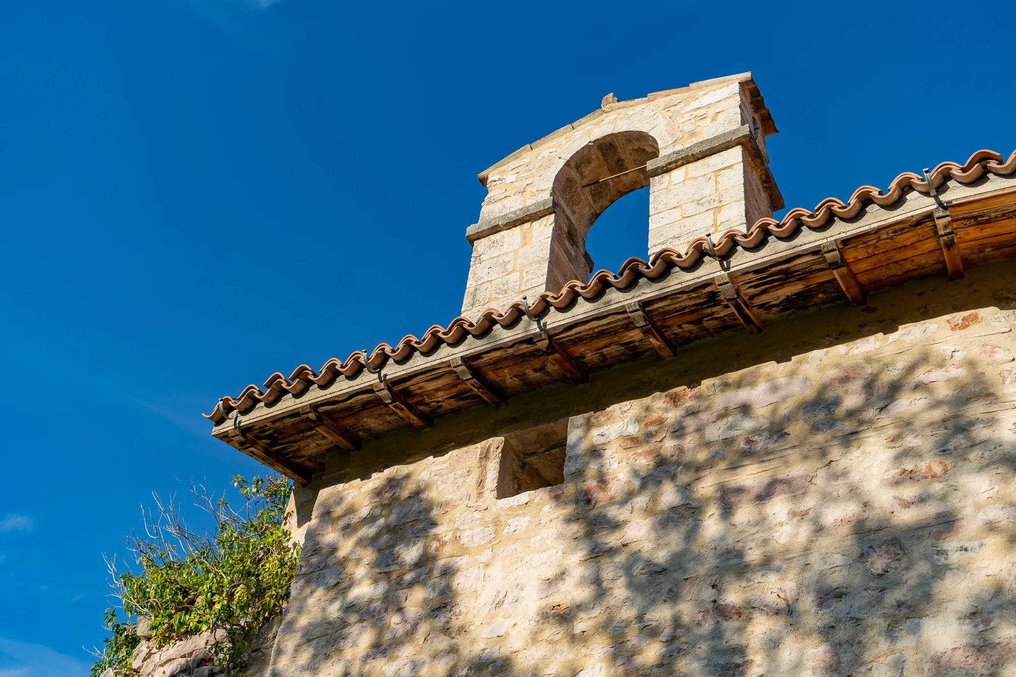 Steinbau mit Glockenturm und Ziegeldach unter blauem Himmel