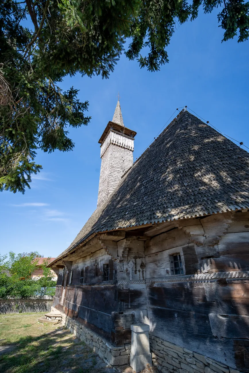 Holzkirche mit spitzen Turm und Schindeldach unter blauem Himmel