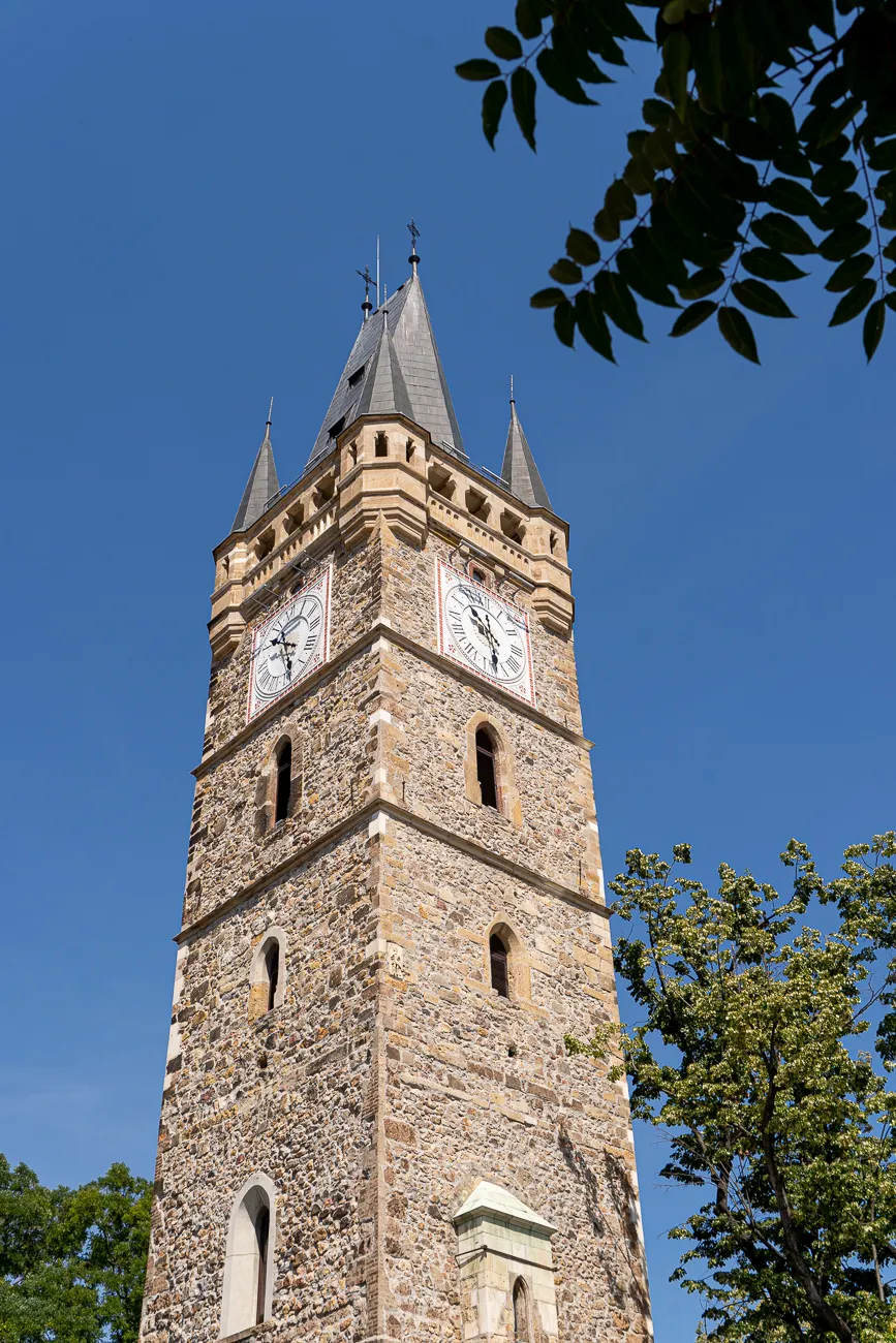 Steinerne Turm mit Uhr und spitzen Dach unter blauem Himmel