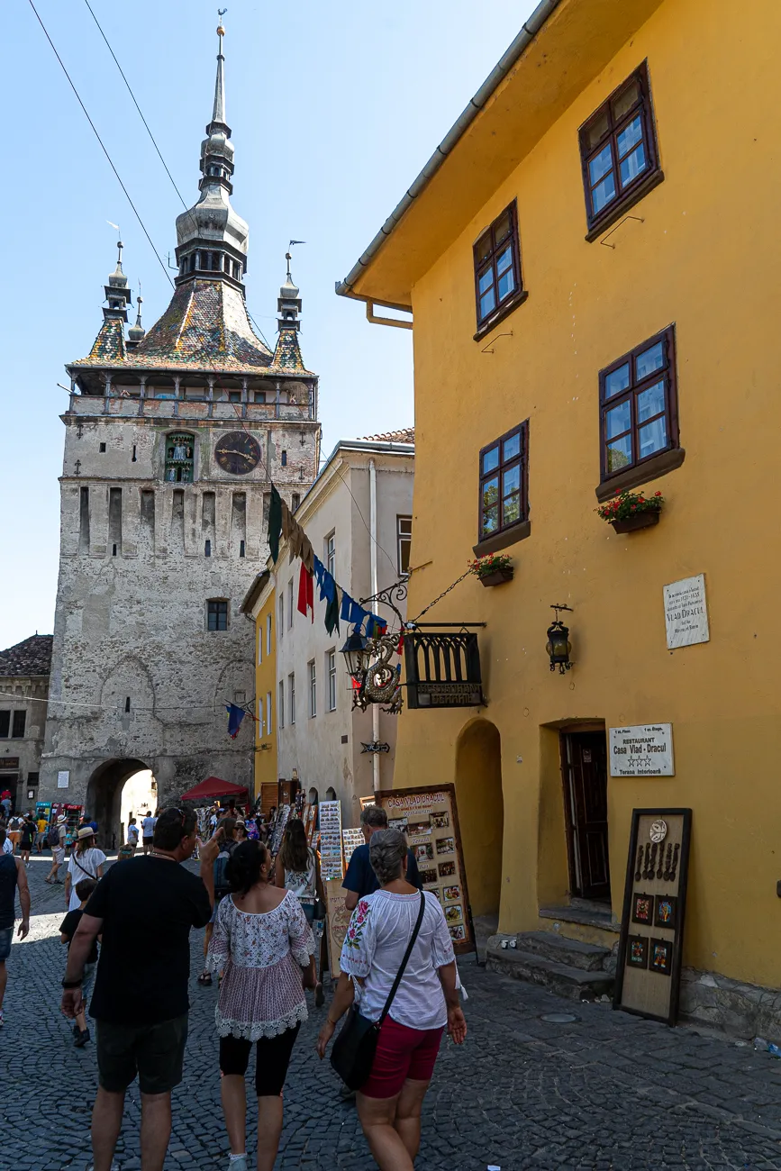 Gelbes Haus mit Balkon und Schild neben historischer Turmruine in Sighișoara
