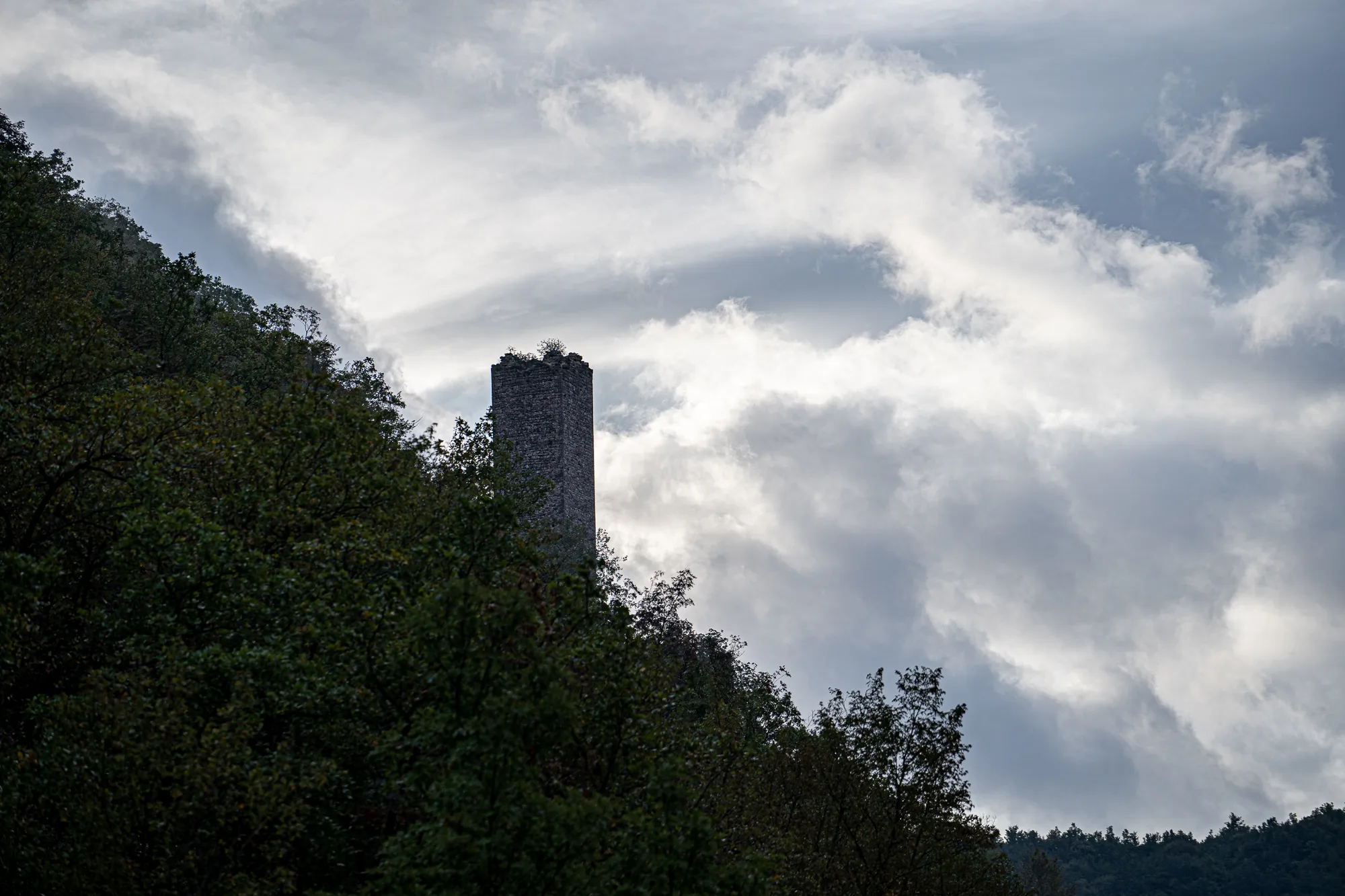 Steinerne Turmruine zwischen Bäumen unter bewölktem Himmel