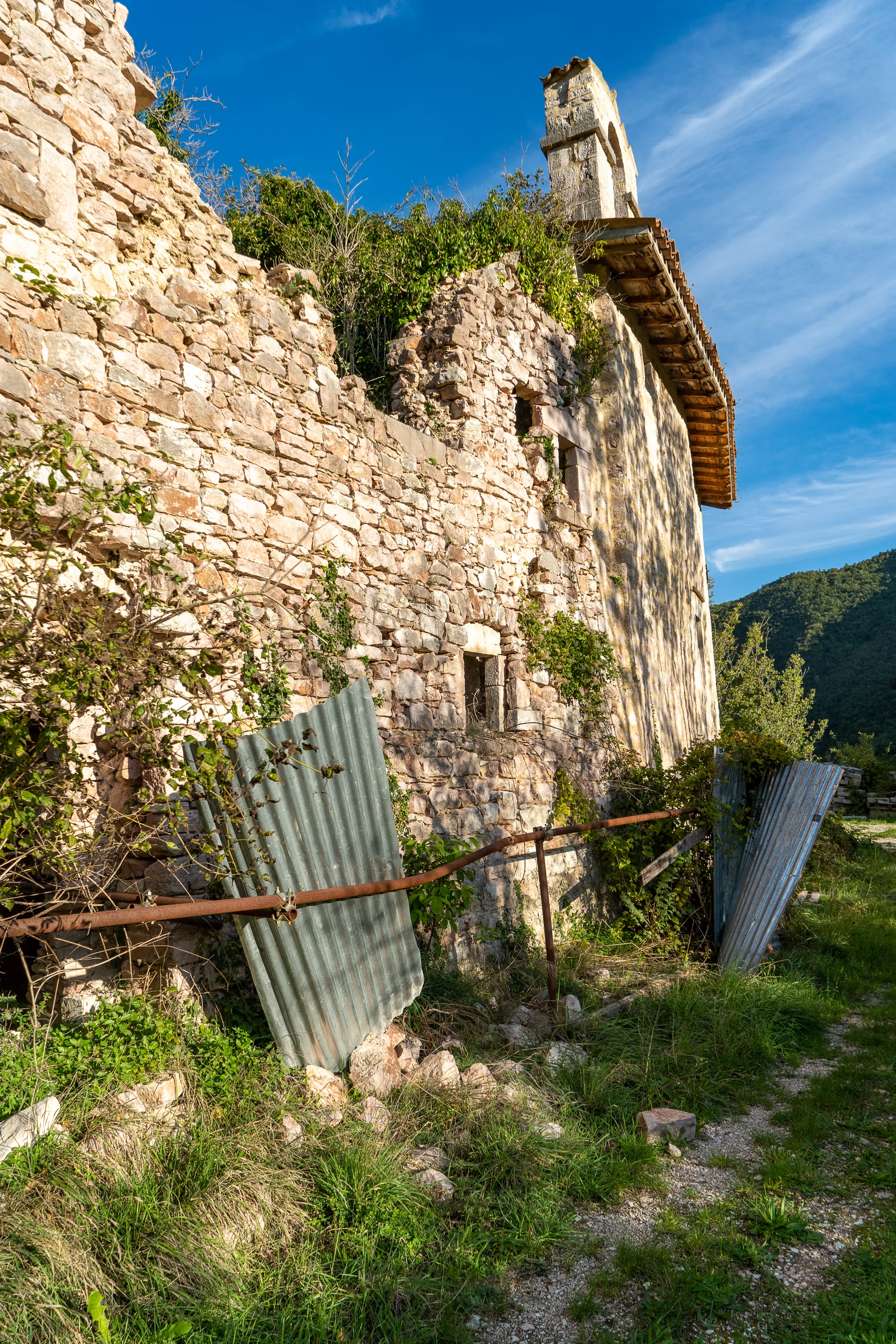 Verfallene Steinmauer mit Dachrest und Grasbewuchs unter blauem Himmel