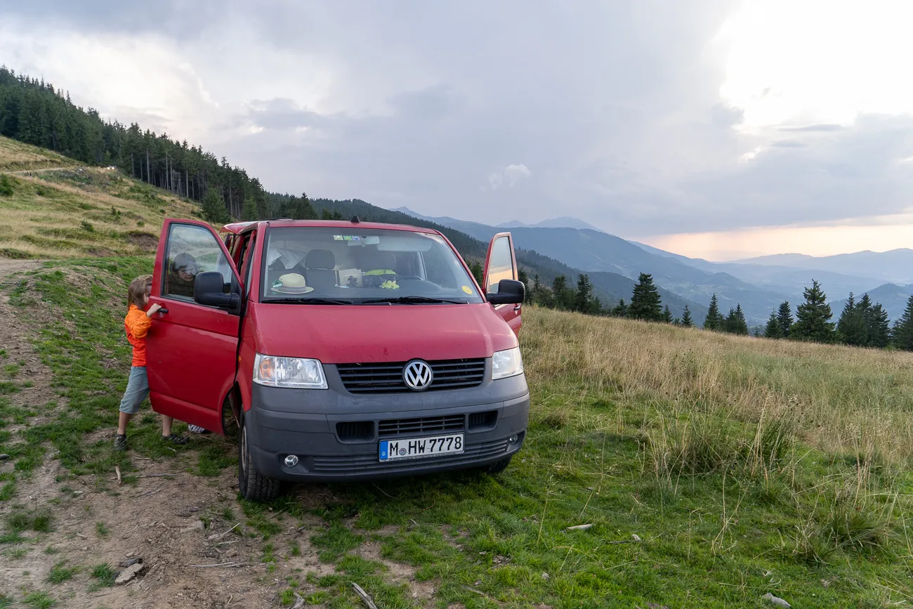 Rote VW-Bus steht auf grünem Hang mit Bergen im Hintergrund