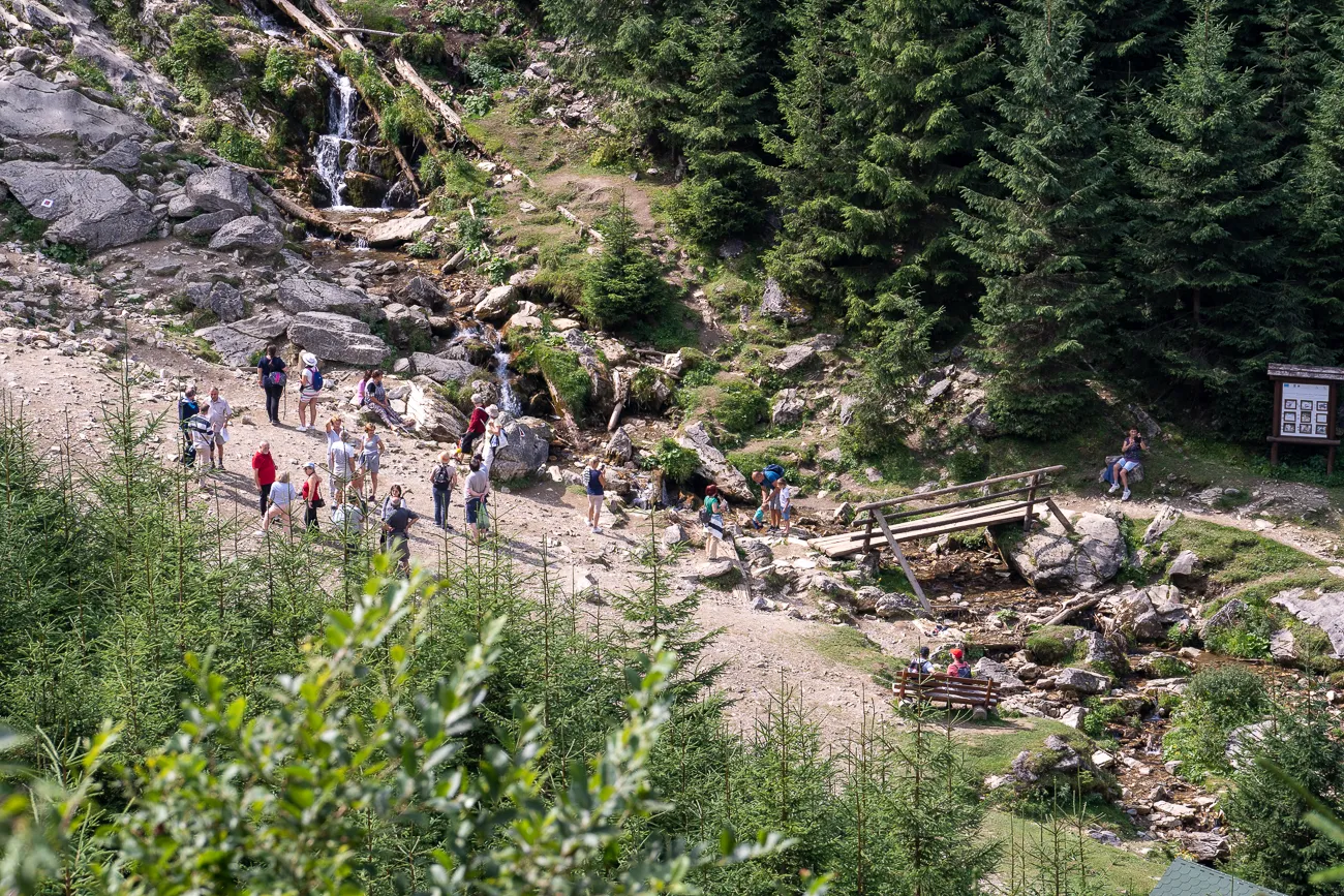 Wasserfall in einem felsigen Tal mit Wanderern und Holzbrücke