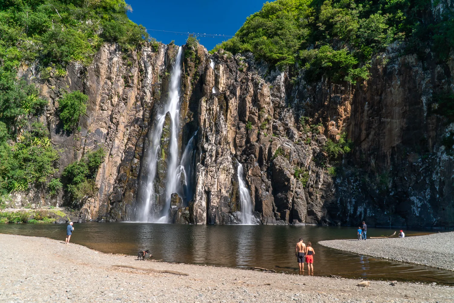 Wasserfall fällt in einen See, Menschen und Hund am Ufer