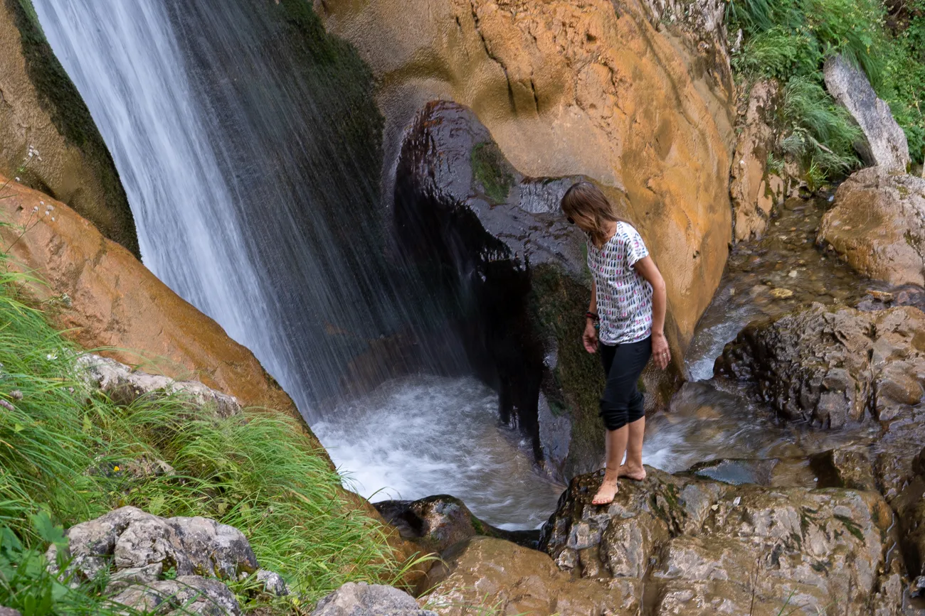Mensch steht auf Stein am Wasserfall mit grünem Gras und Felsen