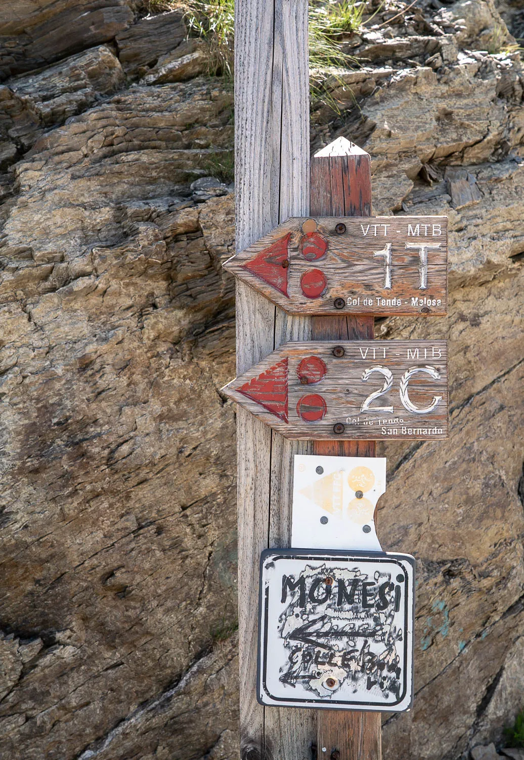 Holzschilder mit Pfeilen und Schriftzug an einem Pfosten vor Felswand