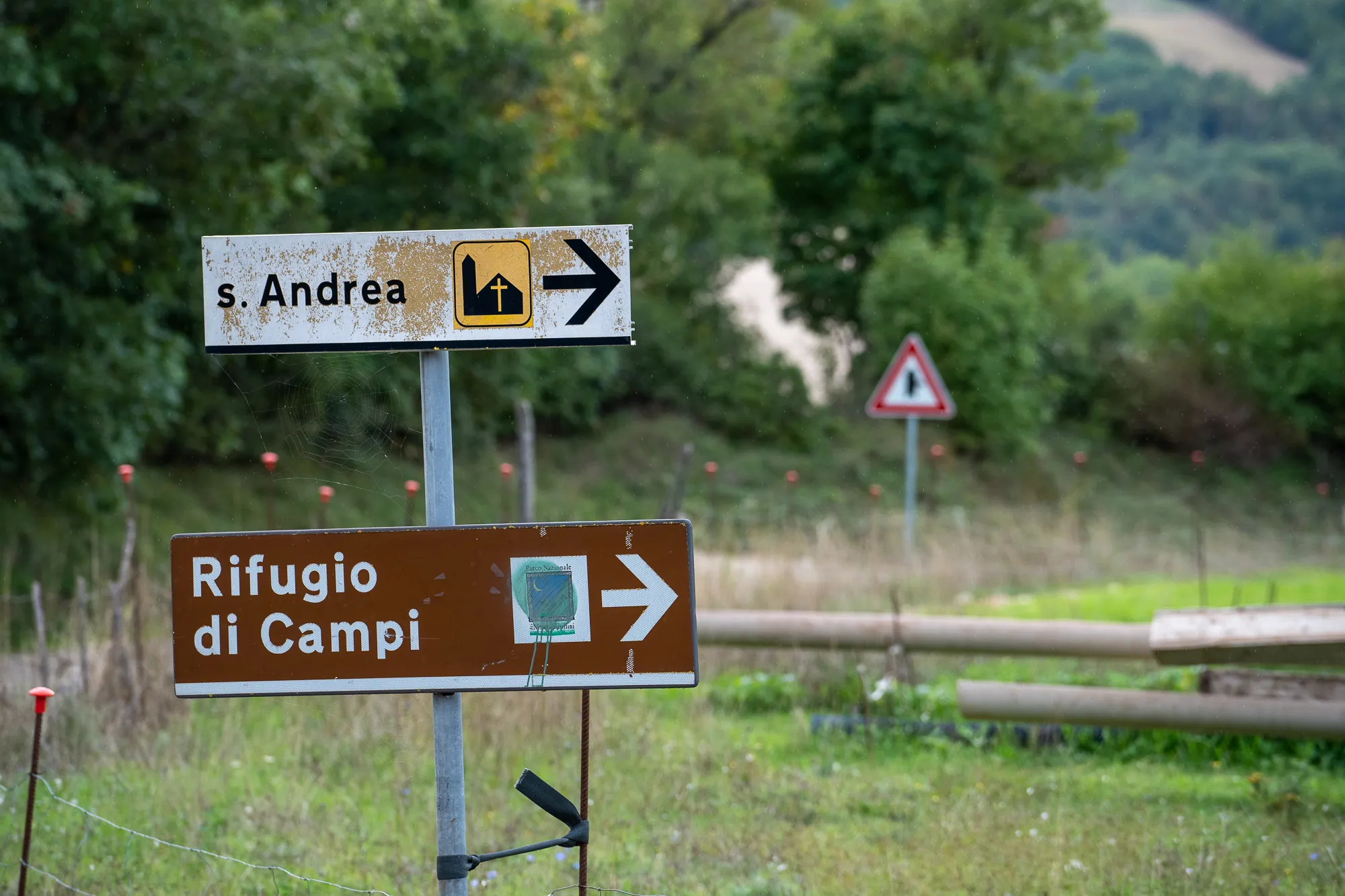 Schilder weisen auf Rifugio di Campi und s. Andrea hin, umgeben von Gras und Bäumen.