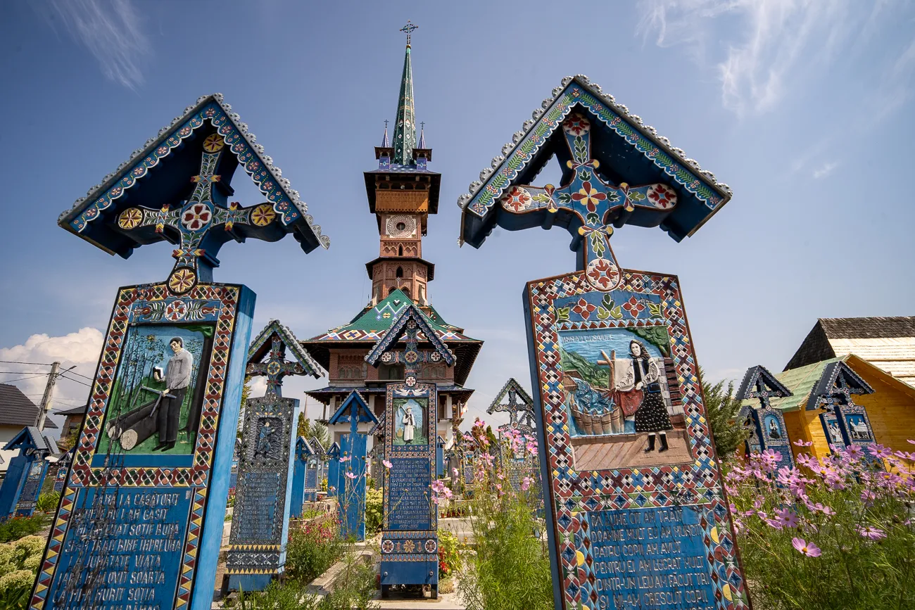 Zwei bunte Holzkreuze mit Bildern und Texten vor einer Kirche im Friedhof.